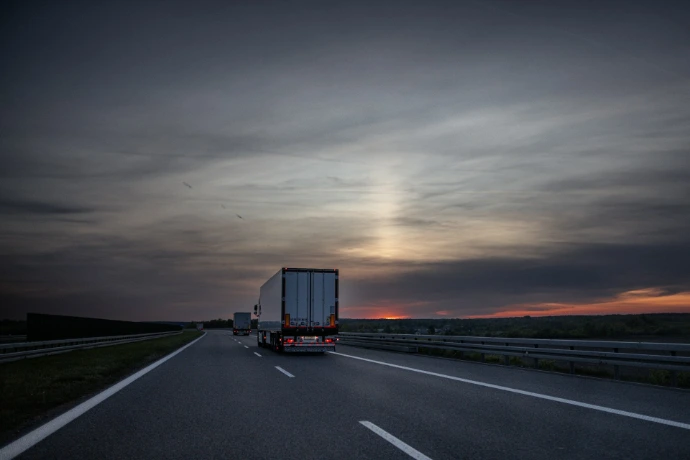 Trucks drive on a highway at sunset.