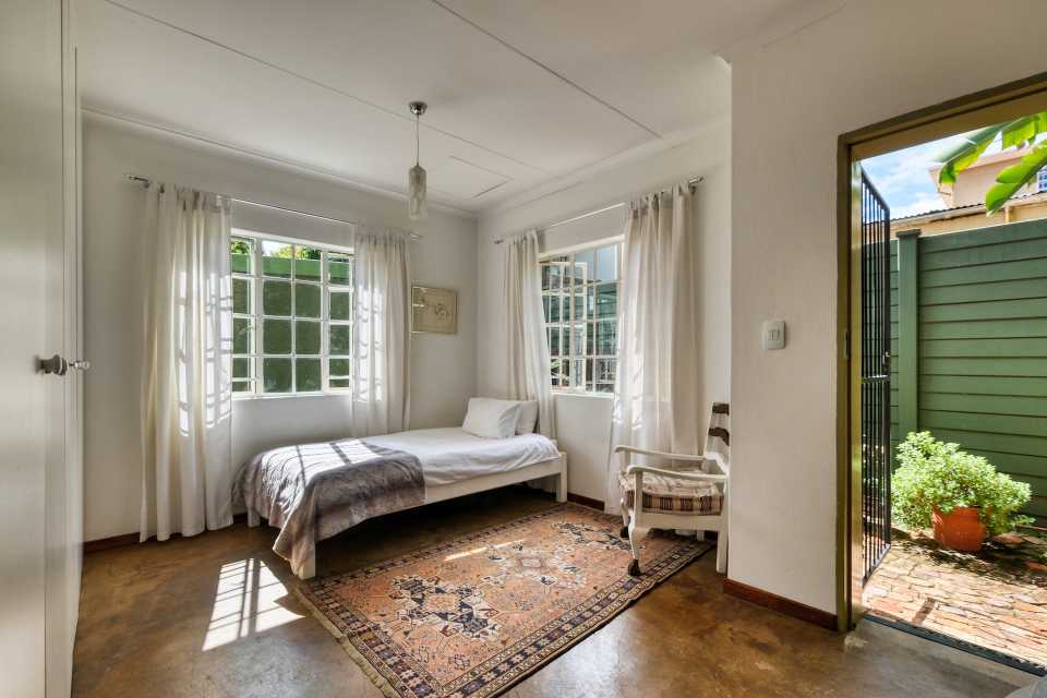 Casa mediteraneana - caracteristici generale - dormitor alb, pat in colt, usa mare deschisa, covor, gard exterior verde