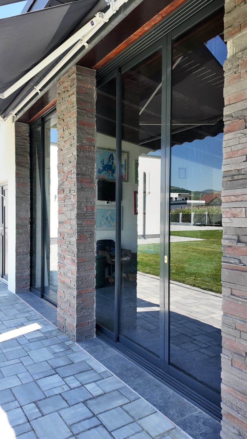 Panou Valedo IS tras lateral lângă stâlpul de piatră, cu mânerul vertical și șina inferioară vizibile la nivelul pavajului