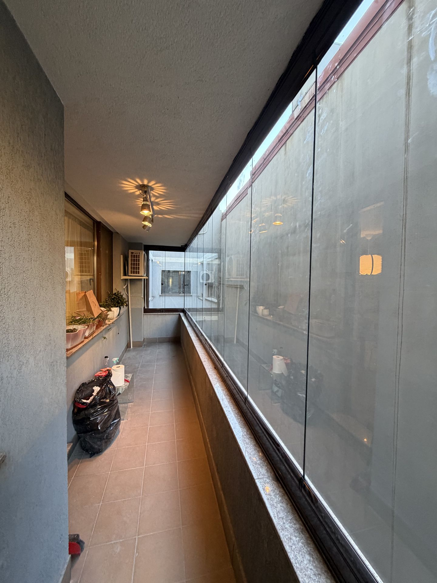Cotul balconului în formă de U închis cu Valedo BKS și latura dinspre apartament, cu ferestrele locuinței și plantele de pe pervaz