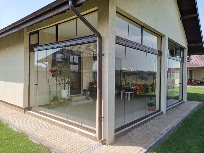Case moderne fara etaj sau cu etaj cum se disting de celelalte - casa bej vazuta de pe colt, cu o terasa inchisa cu sticla